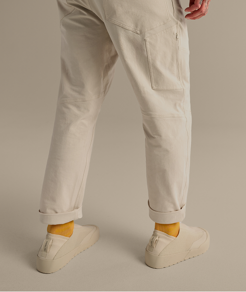 A person wearing light beige pants with rolled cuffs, bright yellow socks, and beige Arc'teryx slip-on shoes.