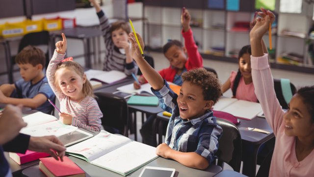 kids raise their hands to answer a question in class