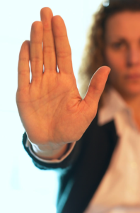 A blurry woman in white blouse and dark jacket holding up a clear hand in the 'stop' position.