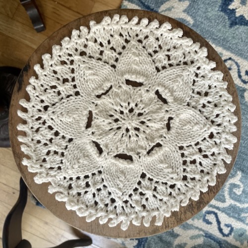 another doily! in peaches and cream and displayed on a round plant stand. floral motif with a picot edging