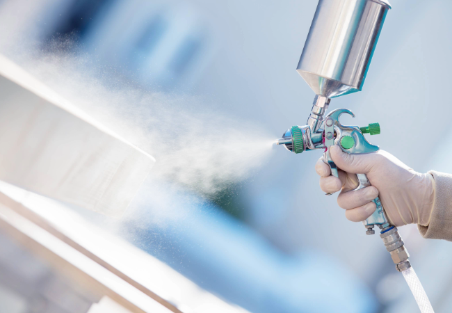 White gloved hand spraying liquid out of a silver and green spray gun
