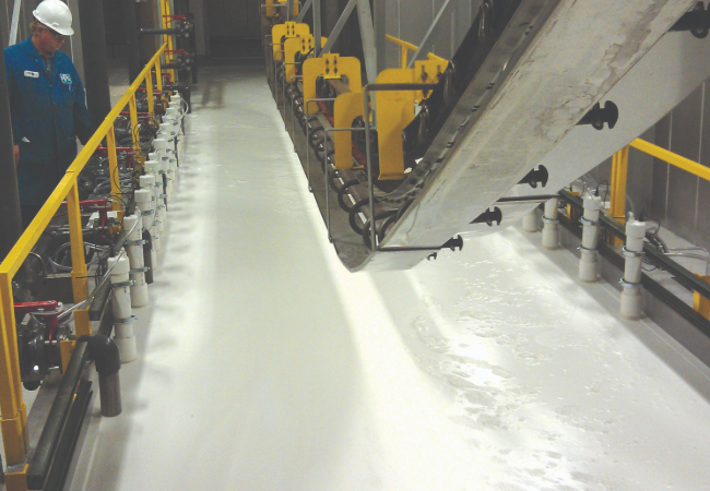 Yellow metal electrocoat line in motion with a worker in overalls and white hard hat watching