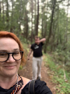 Selfie of me on a redwood trail Leo is visible, blurrily, behind me.