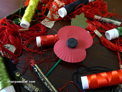 Paper remembrance poppy surrounded by assorted embroidery threads Silk and cotton threads surround a paper remembrance poppy