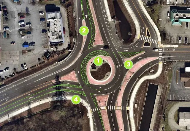 Aerial view of the SR 9/SR 204 roundabout in Lake Stevens with red concrete islands and yellow and white lane striping. Superimposed on the photo are four green circles with the numbers one through four and proposed striping modifications for the roundabout.