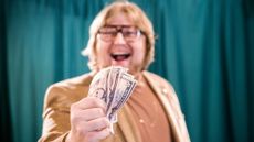 Vintage-looking man wearing a turtleneck with a blazer holding a handful of money
