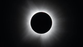 A black circle against a black background surrounded by white wispy tendrils