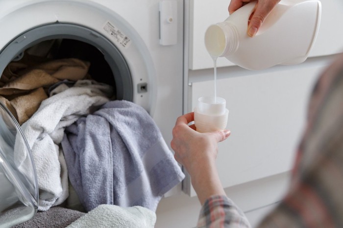 洗濯機の前で液体洗剤をキャップに注ぐ女性