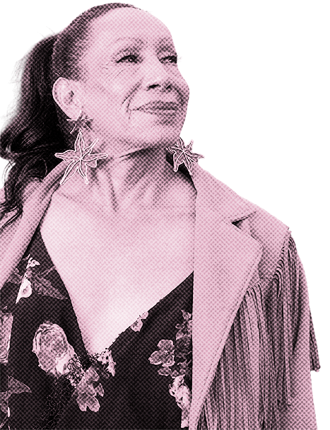 A woman wearing a floral dress and a jacket stands confidently, showcasing her stylish outfit.