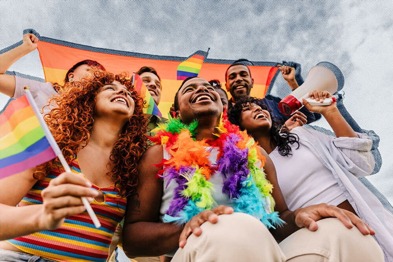 A diverse group of people joyfully holding rainbow flags, celebrating pride and inclusivity in a vibrant outdoor setting.