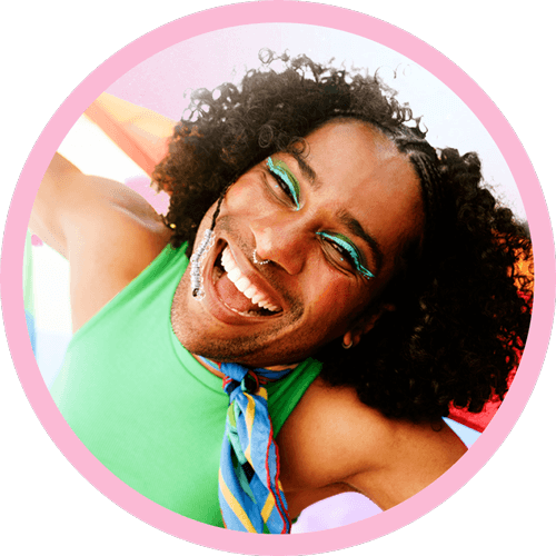 A man with curly hair stands confidently with a Pride flag, highlighting his unique hairstyle in a relaxed environment.