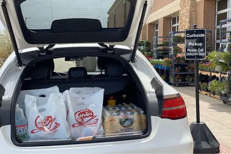 An image of the back of white SUV with the backdoor ajar, with bags of groceries and a case of water within it.