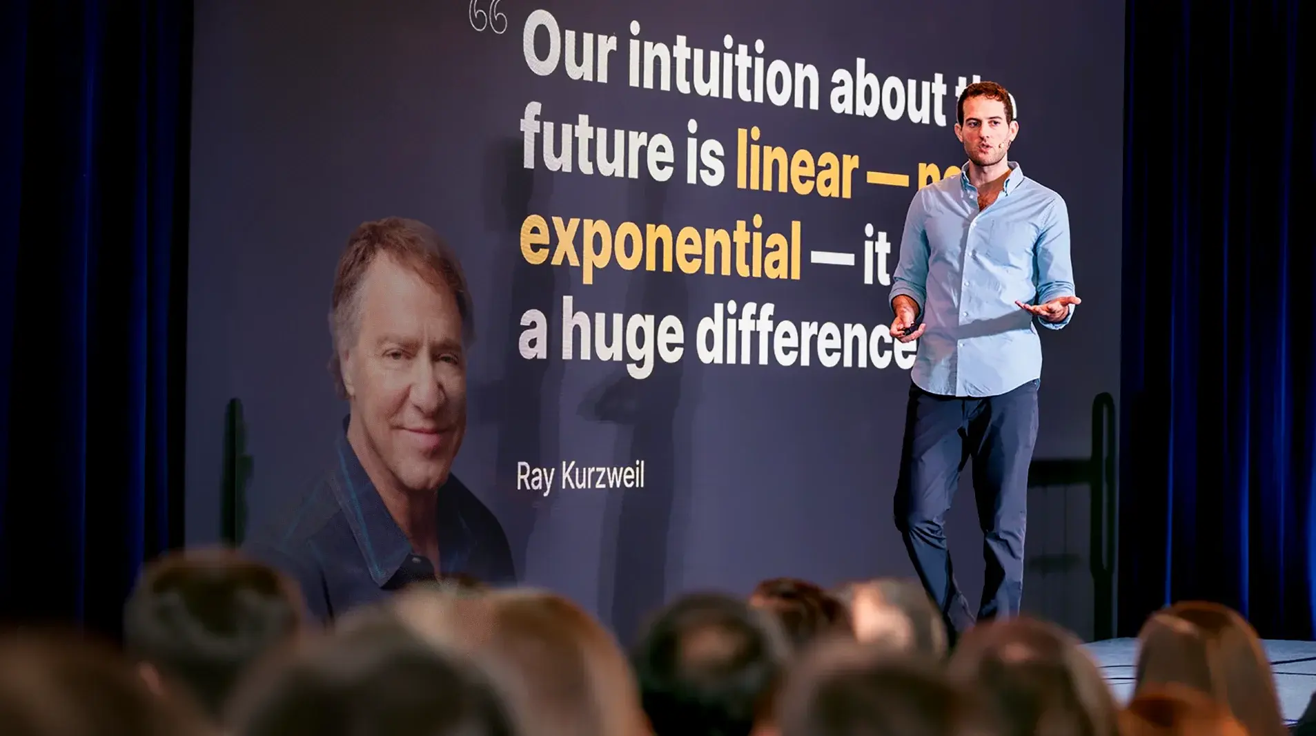 Man in blue shirt speaking on stage with quote on screen about future being exponential by Ray Kurzweil.