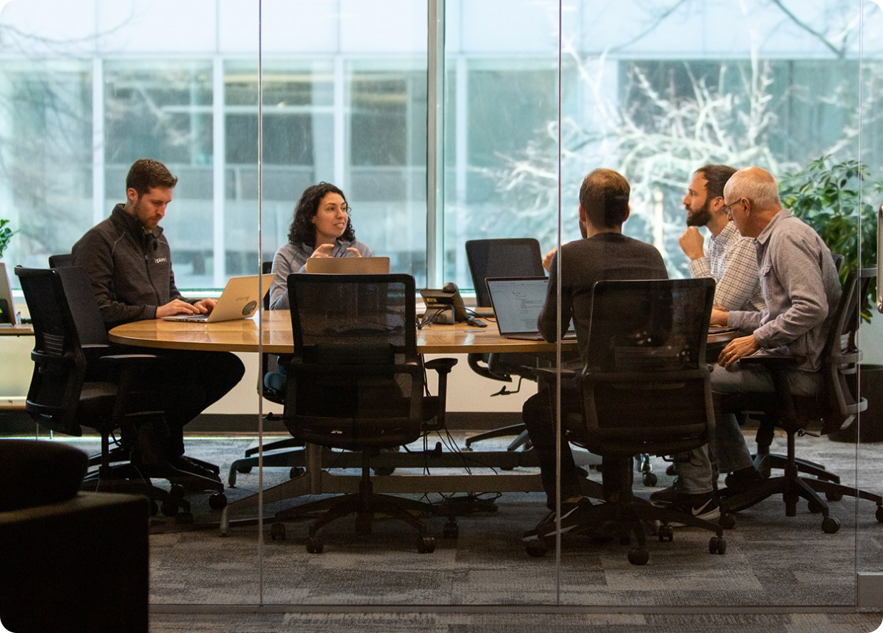 A group of Galois employees sitting around a wooden table in a glass conference room.