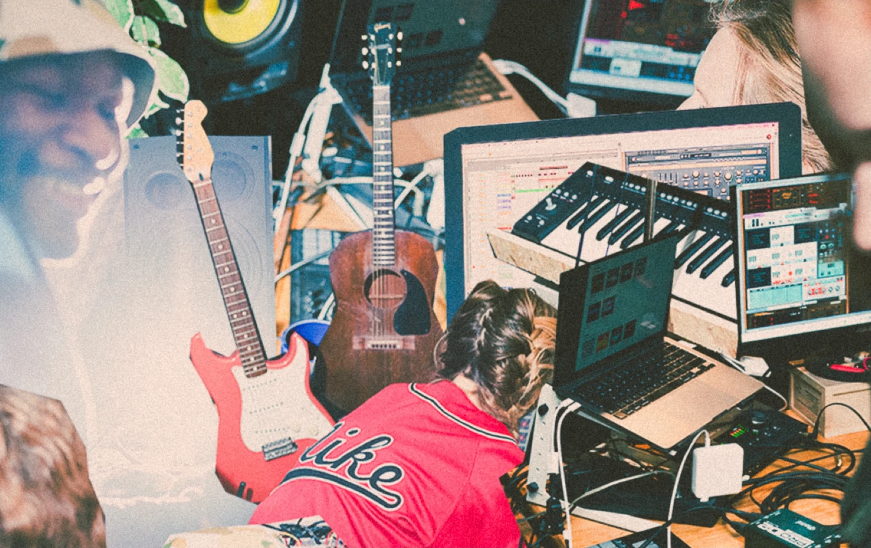 People working in a music studio surrounded by guitars, computers, and audio equipment.