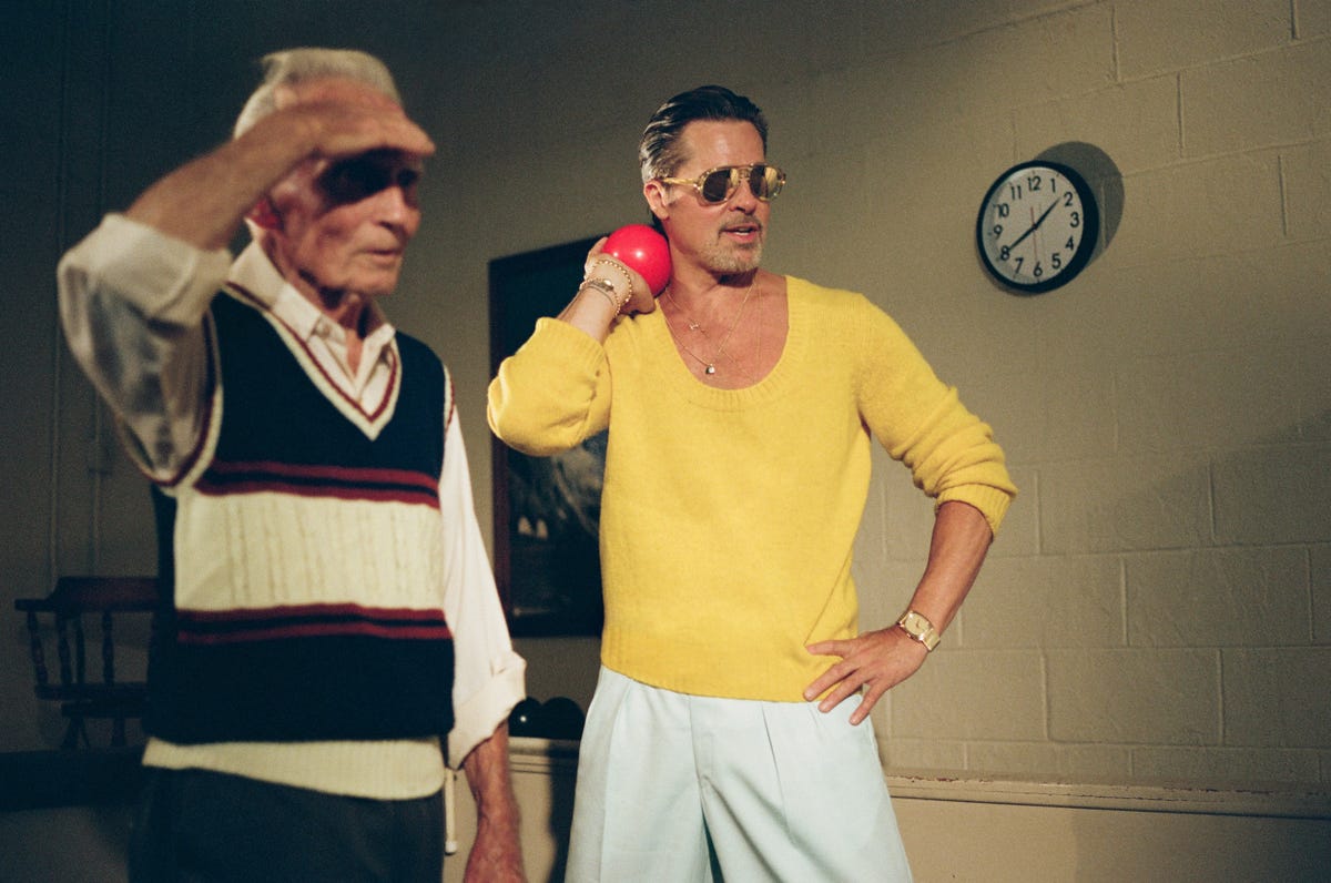 Two men in casual attire, one holding a red ball, standing indoors with a clock on the wall in the background. Two men in casual attire, one holding a red ball, standing indoors with a clock on the wall in the background.