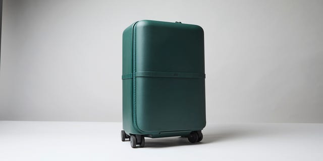 Dark green July suitcase with a smooth finish and wheels, positioned against a light gray background. Dark green July suitcase with a smooth finish and wheels, positioned against a light gray background.