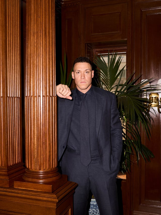 Man in a dark suit standing next to wooden pillars in a formal setting. Man in a dark suit standing next to wooden pillars in a formal setting.
