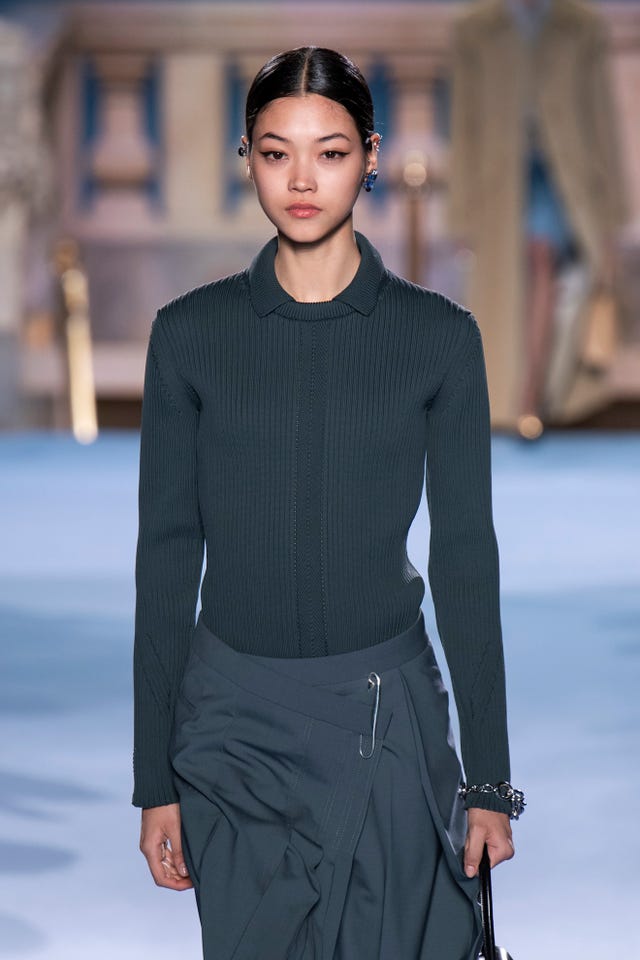 Model wearing a ribbed sweater and draped skirt on runway. Model wearing a ribbed sweater and draped skirt on runway.