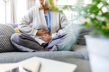 Woman having stomach ache sitting on sofa at home Woman having stomach ache sitting on sofa at home