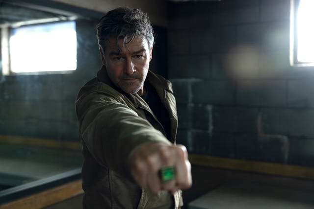 Man in a jacket extending his arm, displaying a green ring, set in an industrial environment with natural light. Man in a jacket extending his arm, displaying a green ring, set in an industrial environment with natural light.