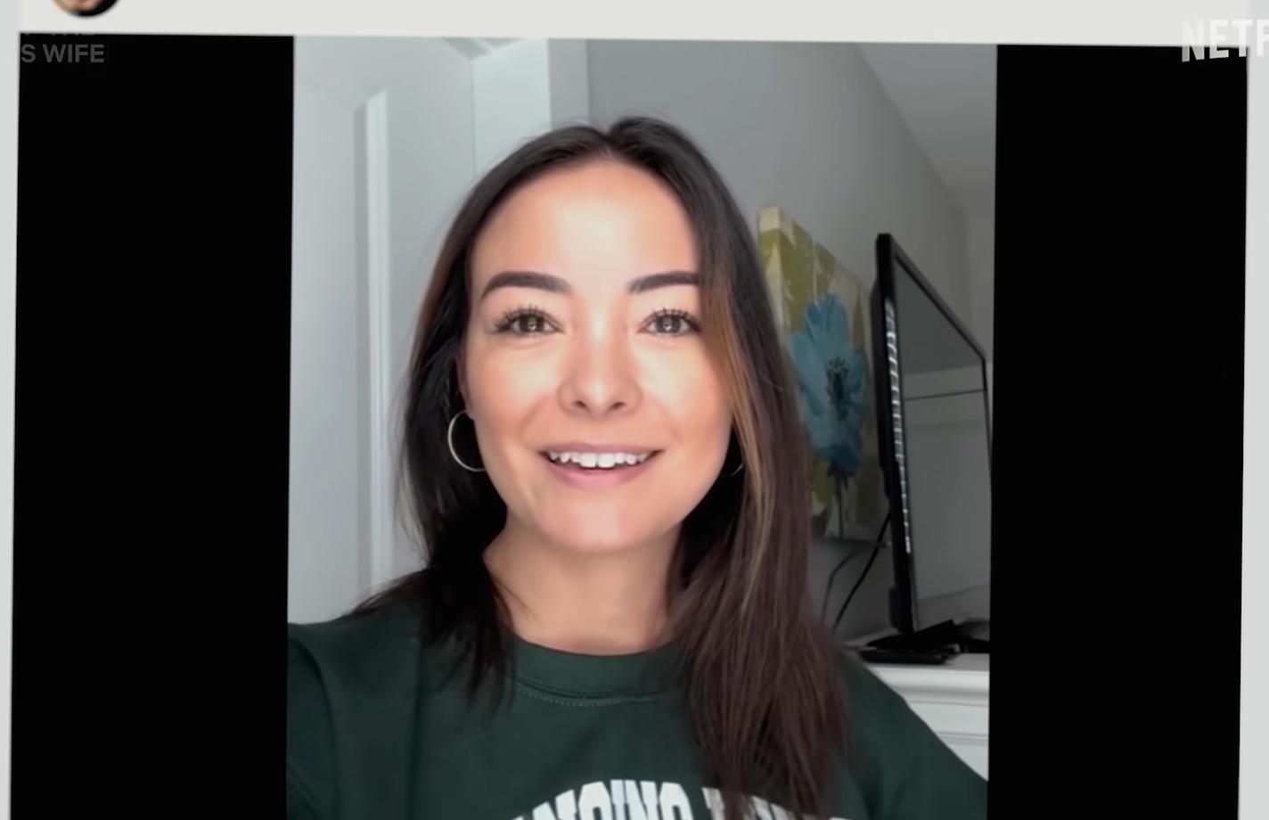 Smiling woman wearing a green sweatshirt, standing in a bright room with a mirror and artwork in the background. Smiling woman wearing a green sweatshirt, standing in a bright room with a mirror and artwork in the background.