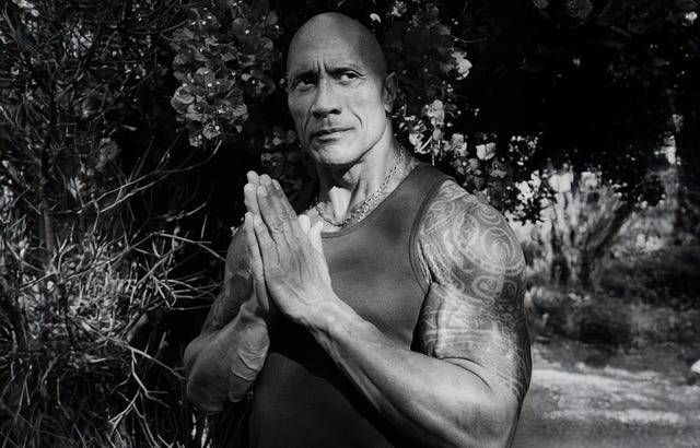 Person with tattoos, in a sleeveless shirt, standing with hands together in front of foliage. Person with tattoos, in a sleeveless shirt, standing with hands together in front of foliage.