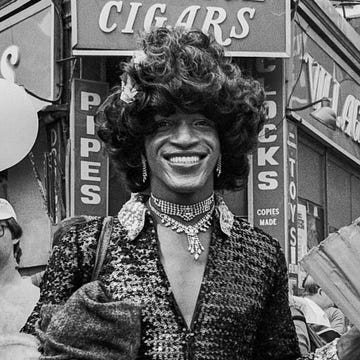 Marsha P. Johnson at a 1982 Pride March marsha p johnson in dark outfit and black hair smiles as she stands on the corner of christopher street and 7th avenue during the pride march