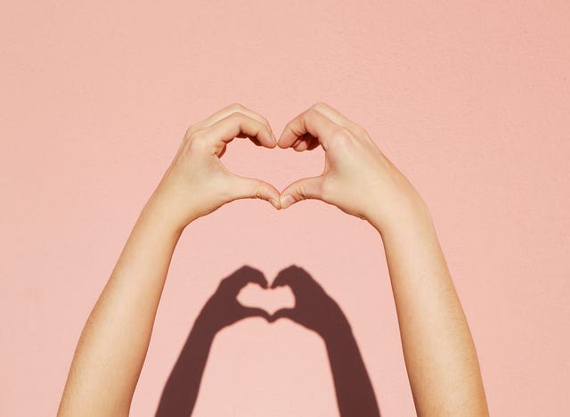 a hand making a heart a hand making a heart shape in front of a pink wall with a shadow of the hand