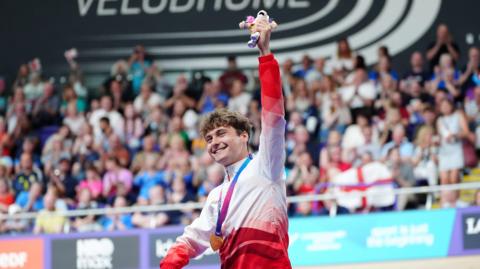 Matthew Robertson holds up his mascot with his gold medal around his neck at the Sir Chris Hoy Velodrome