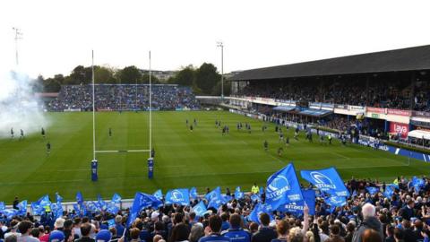 Leinster fans wave blue flags as smoke from fireworks drifts across their home ground ahead of a game against Connacht in 2024