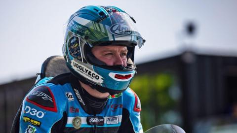 A head and shoulders shot of Daniel Ingham on his motorcycle. He is wearing a light blue helmet and leathers, which have sponsors' logos on them.