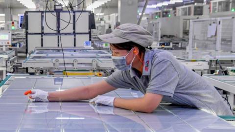 A woman leans over a large sheet of solar panel modules at a factory in Jinhua, Zhejiang Province of China.