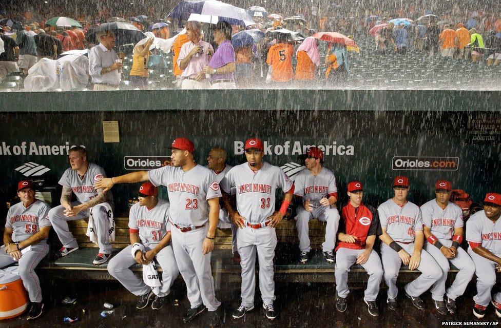 Members of the Cincinnati Reds watch from the dugout as heavy rain falls