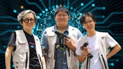 Three women wearing work vests look into the camera, with two of them (the middle and the right) holding drills. The background shows blue electronic waves