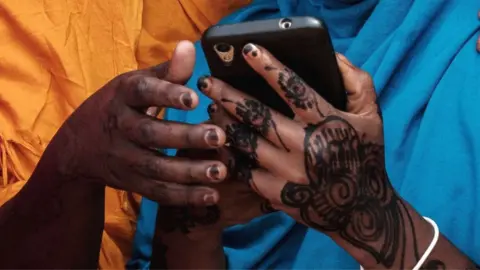 A close up of a young woman from Somalia with hennaed hands holding a mobile