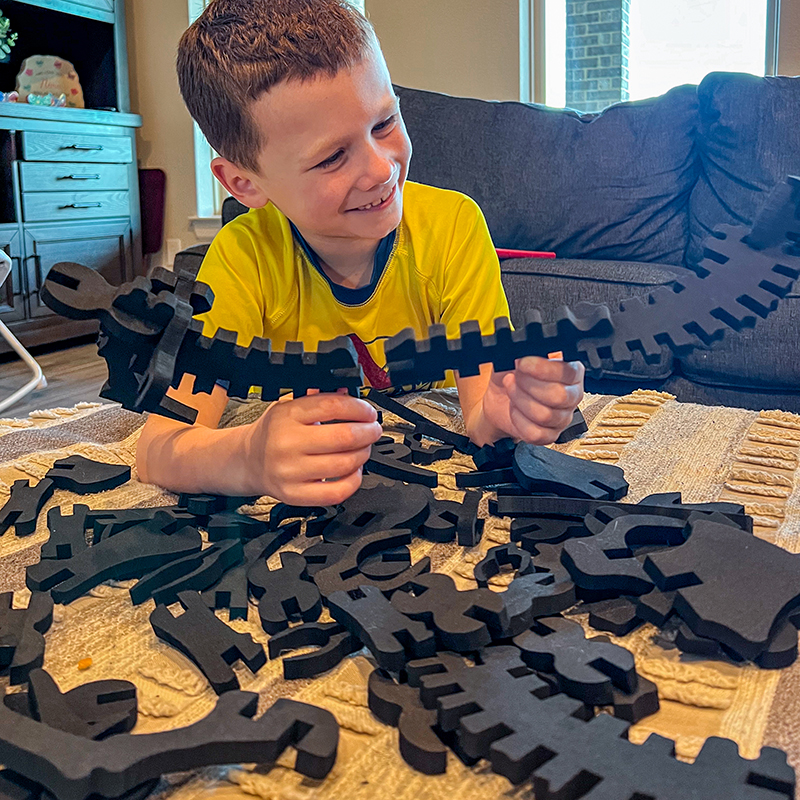 Child engaging in STEM-inspired play with Imagination Playground's foam dinosaur bones. This loose-part play set allows kids to construct dinosaur skeletons, promoting teamwork and creativity in classrooms or educational play spaces.