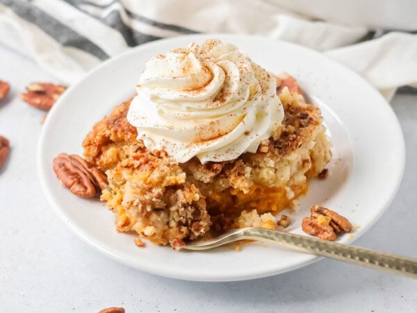 Pumpkin Dump Cake slice on white plate with whipped cream on top.