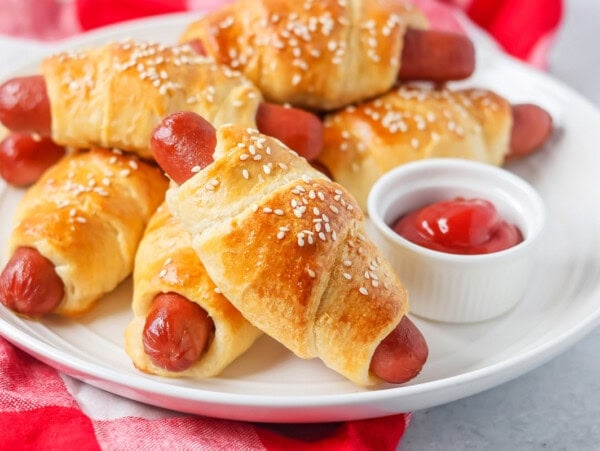 Easy pigs in a blanket stacked on each other on white plate.