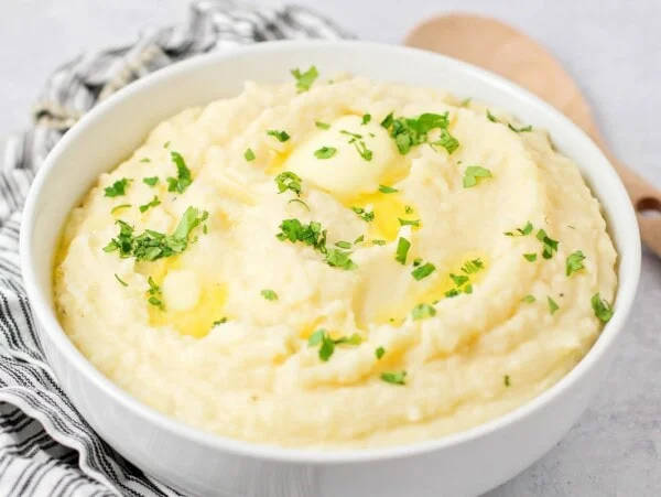 A bowl of crock pot mashed potatoes topped with butter and herbs.
