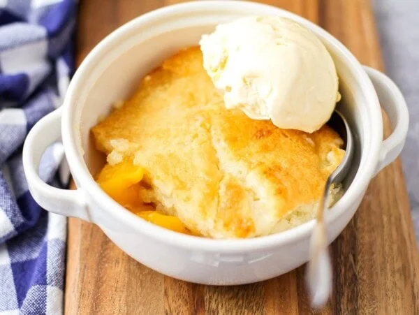Scoop of easy peach cobbler in a white bowl with ice cream on top.