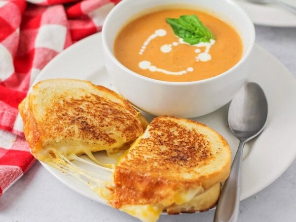 Grilled cheese recipe pulled apart on white plate served with tomato soup.