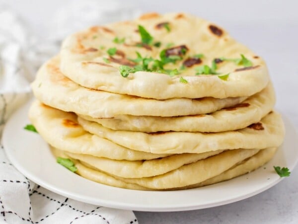 Homemade naan bread stacked on top of each other on white plate.