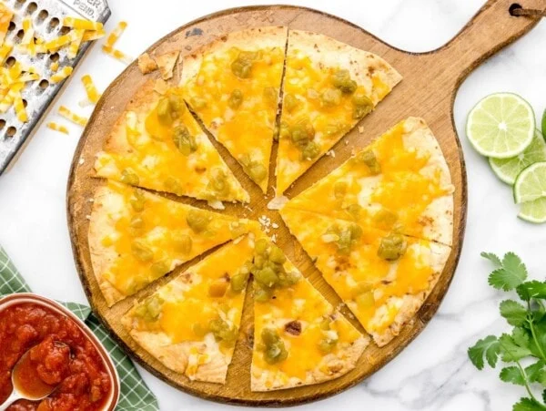 A sliced cheese crisp topped with green chilis.