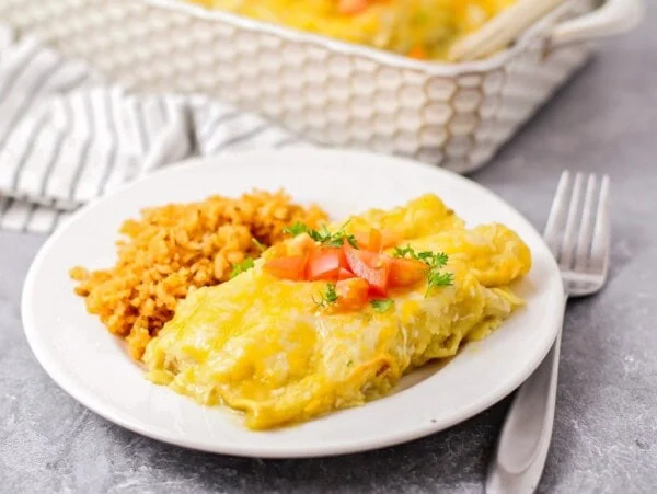 Easy chicken enchiladas on white dish with Spanish Rice.