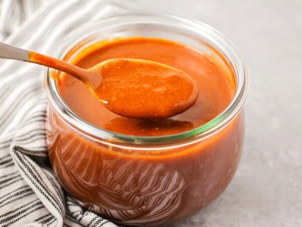 Homemade enchilada sauce recipe being spooned out of glass jar.