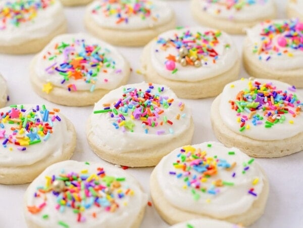 Frosted sugar cookies on parchment paper with sprinkles on top.