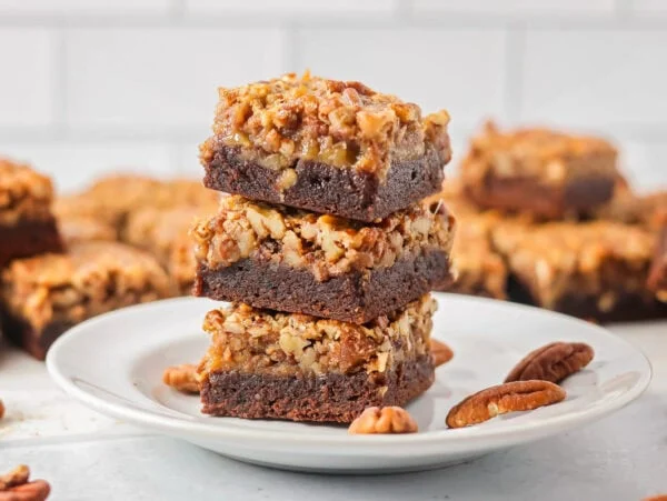Three pecan pie brownies cut and stacked on a plate.