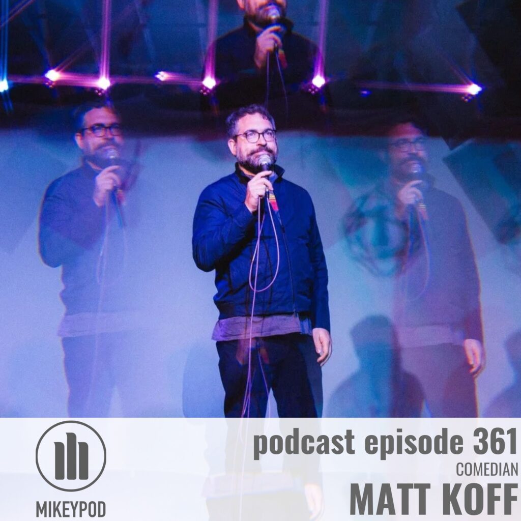 MikeyPod episode 361 cover art: Matt Koff, comedian, performing on stage under blue and purple neon lighting, holding a microphone. He has short dark hair, a beard, and wears glasses and a dark blue zip-up jacket.