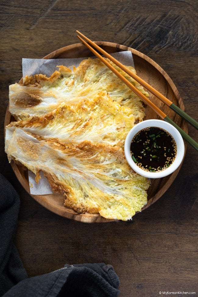 Baechujeon served on a wooden plate with chopsticks and a bowl of dipping sauce.
